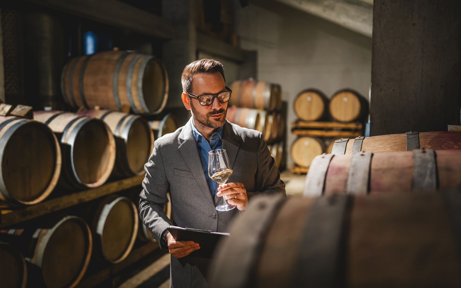 Adult man winemaker hold glass stand between the barrels in cellar