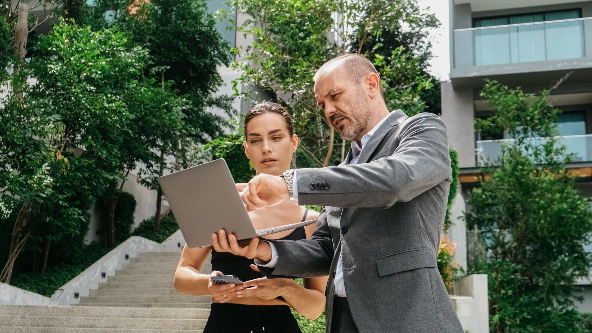 A businessman and a female engineer stand by a modern building, discussing a new construction project. Their enthusiasm for ideas reflects a team spirit and a drive for innovation.